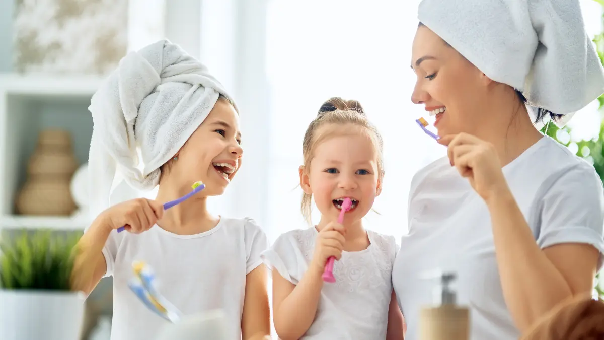 Mamma e figlie sorridenti si lavano i denti insieme, promuovendo l’igiene orale in famiglia