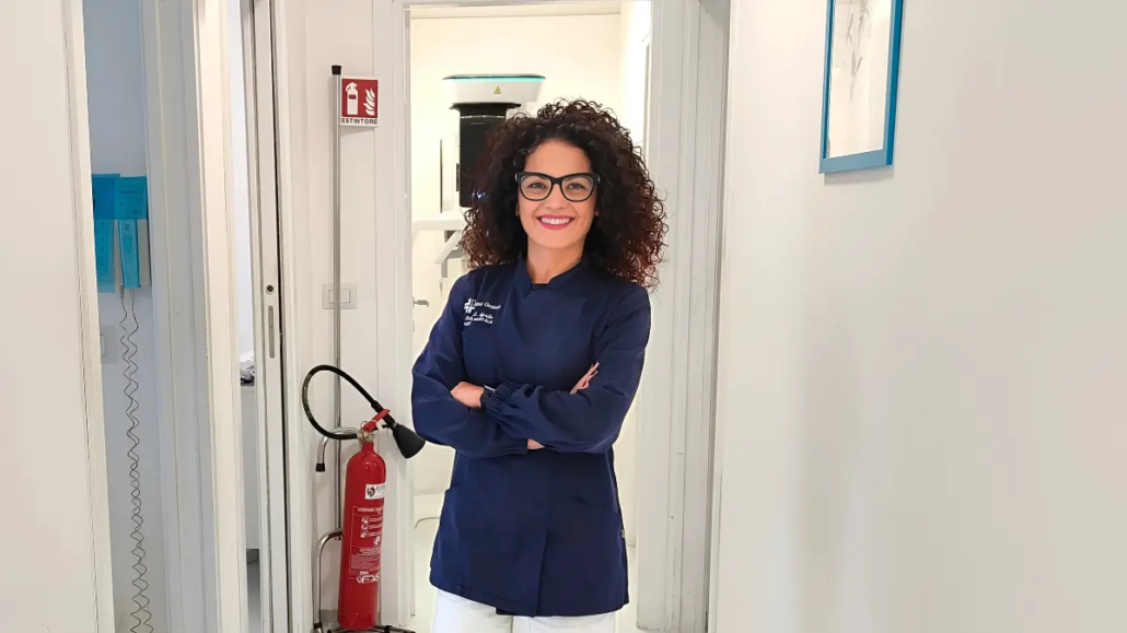 Dottoressa Carmen Aprile sorridente con camice e braccia conserte nel corridoio dello studio dentistico.
